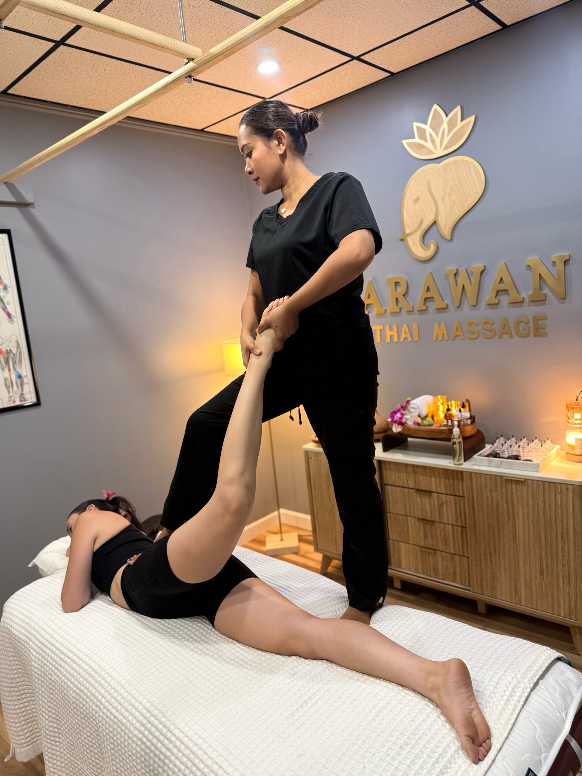A female masseuse standing and pulling a woman's leg up.
